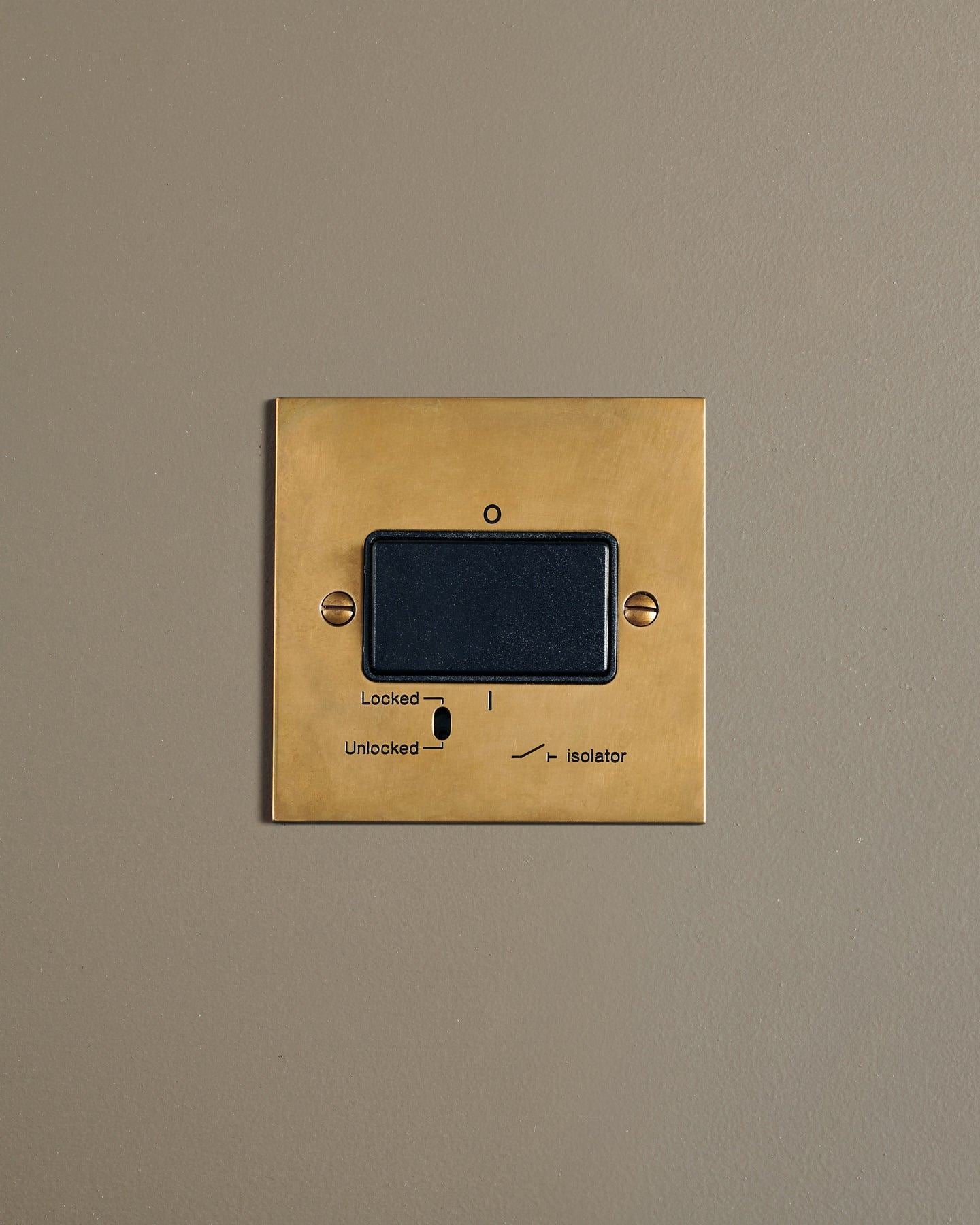 A straight-on view of a classic extractor fan isolator switch a warm burnished brass finish.