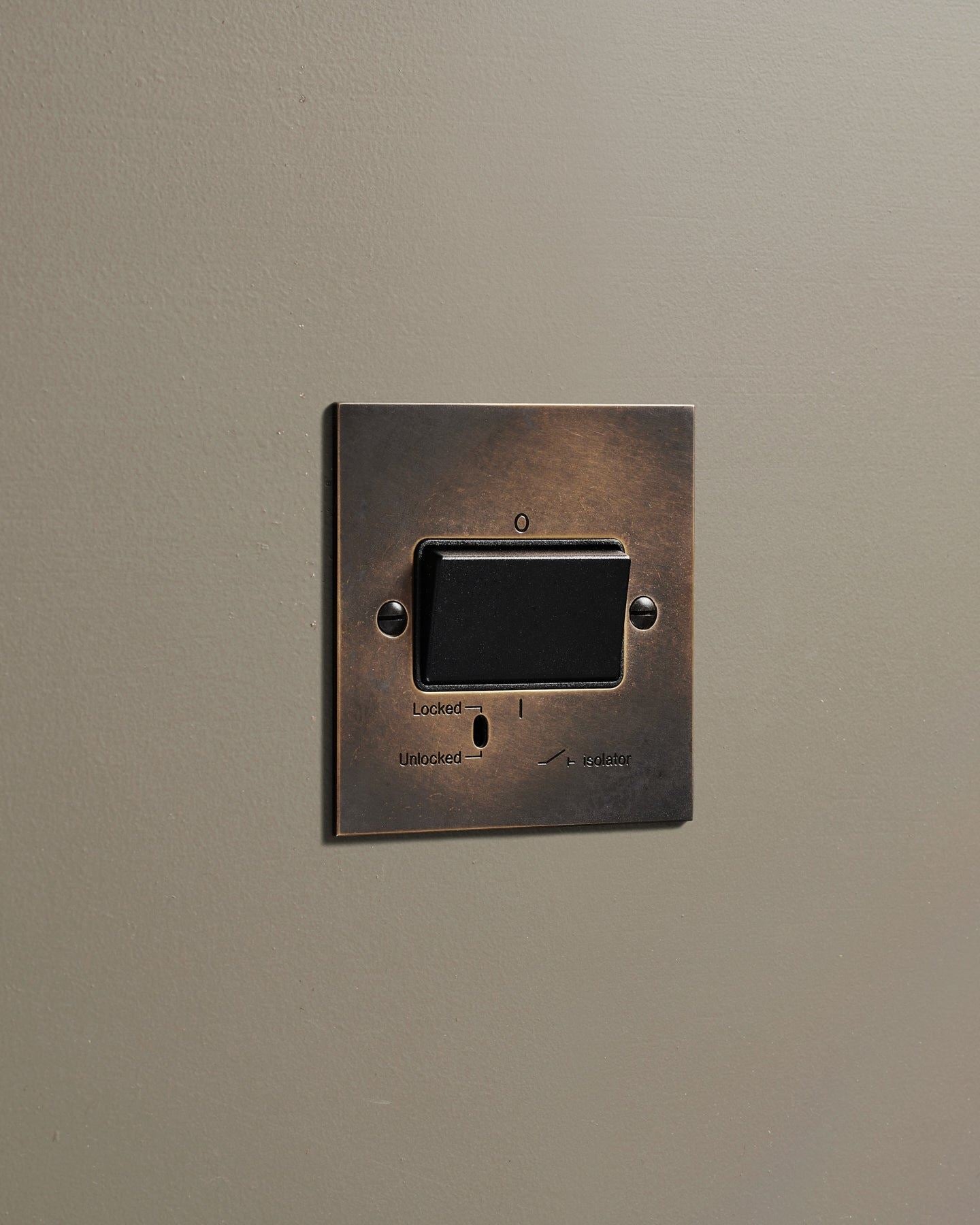 An oblique view of a classic extractor fan isolator switch in a dark oxidised brass finish.
