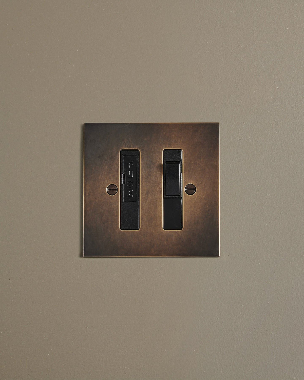 A straight-on view of a classic fused connection switch in a dark oxidised brass finish. TEST
