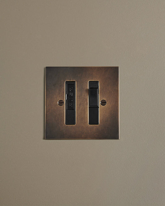 A straight-on view of a classic fused connection switch in a dark oxidised brass finish.