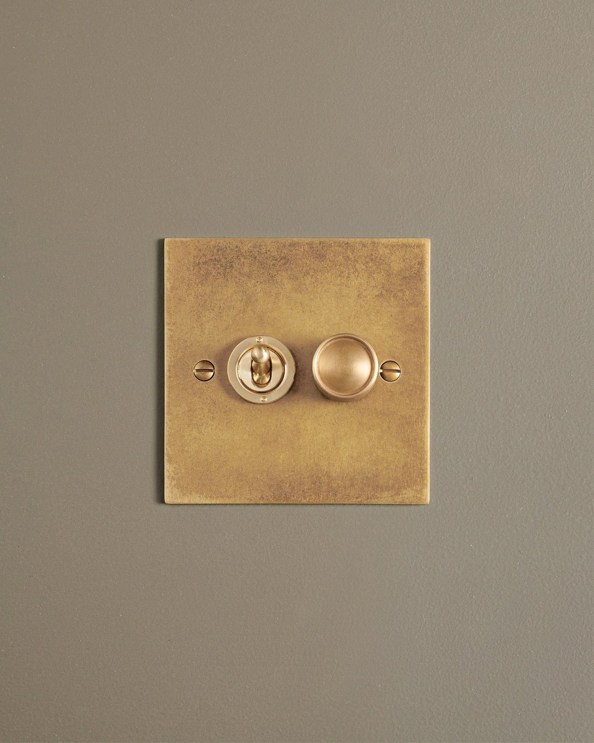 A straight-on view of a 2 gang classic toggle and dimmer mixed switch in a mottled aged brass finish. TEST