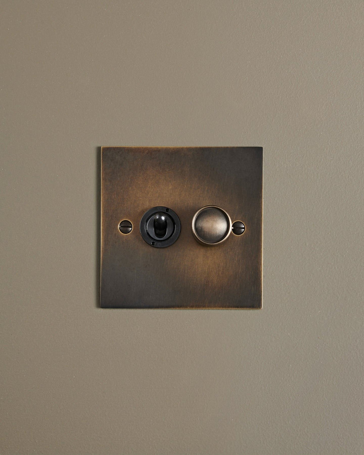 A straight-on view of a 2 gang classic toggle and dimmer mixed switch in a dark oxidised brass finish. TEST