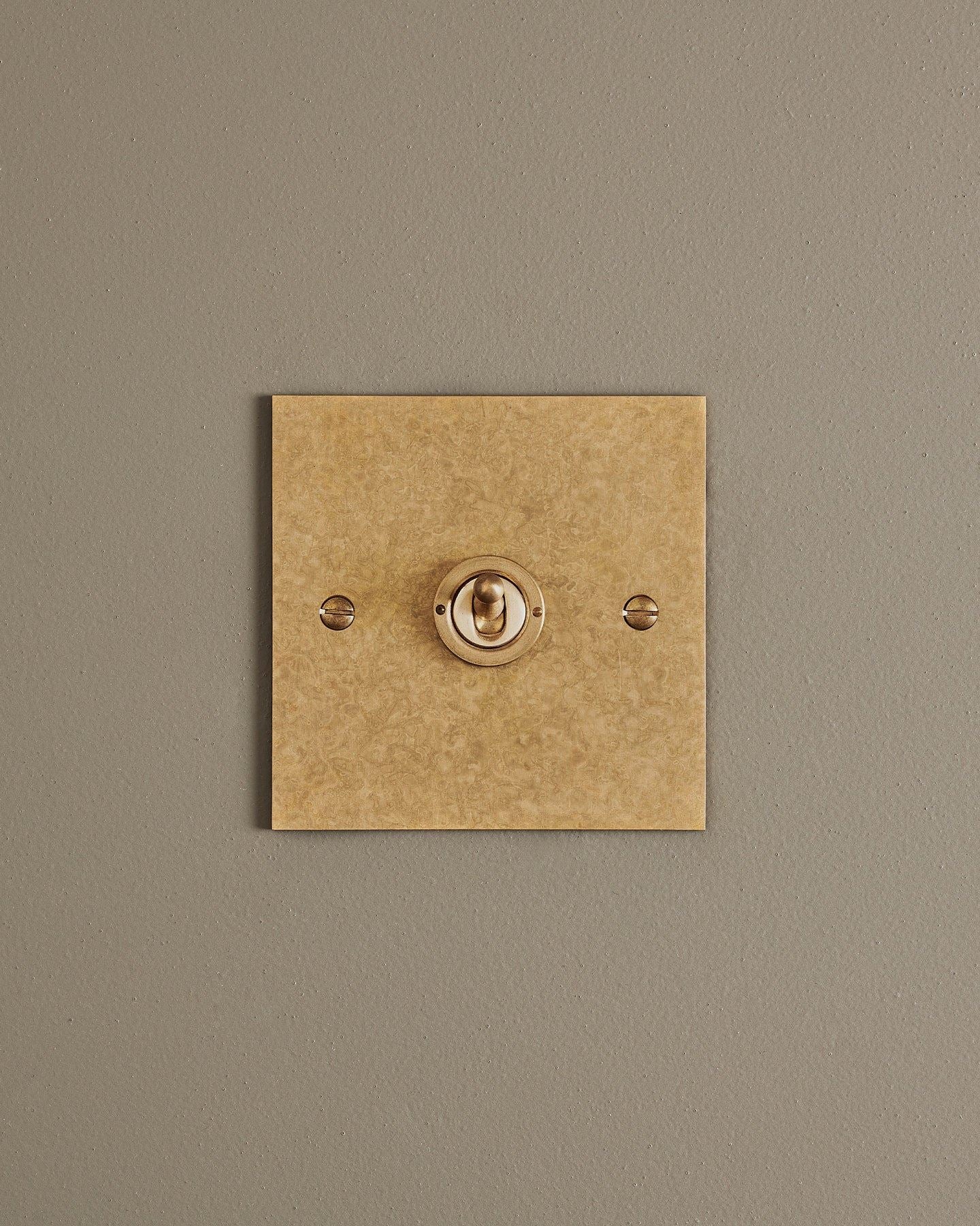A straight-on view of a 1 gang classic toggle switch in a mottled aged brass finish.