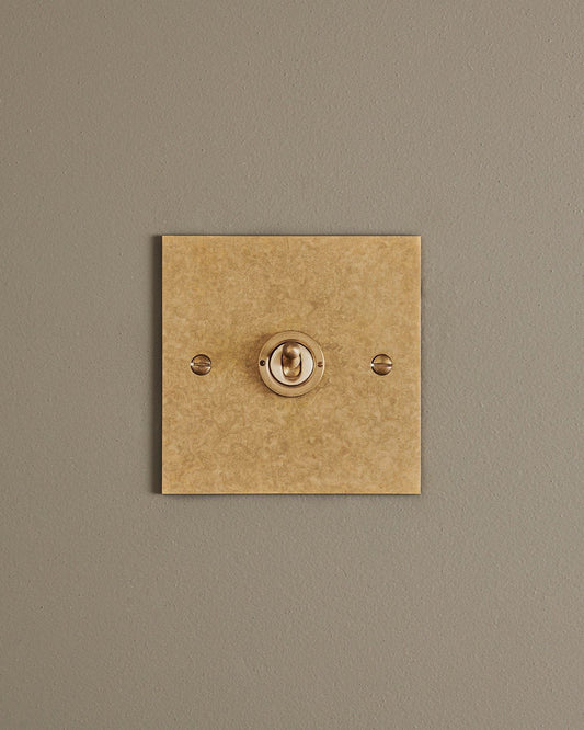 A straight-on view of a 1 gang classic toggle switch in a mottled aged brass finish.