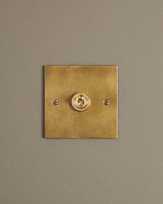 A straight-on view of a 1 gang classic toggle switch in a warm burnished brass finish.