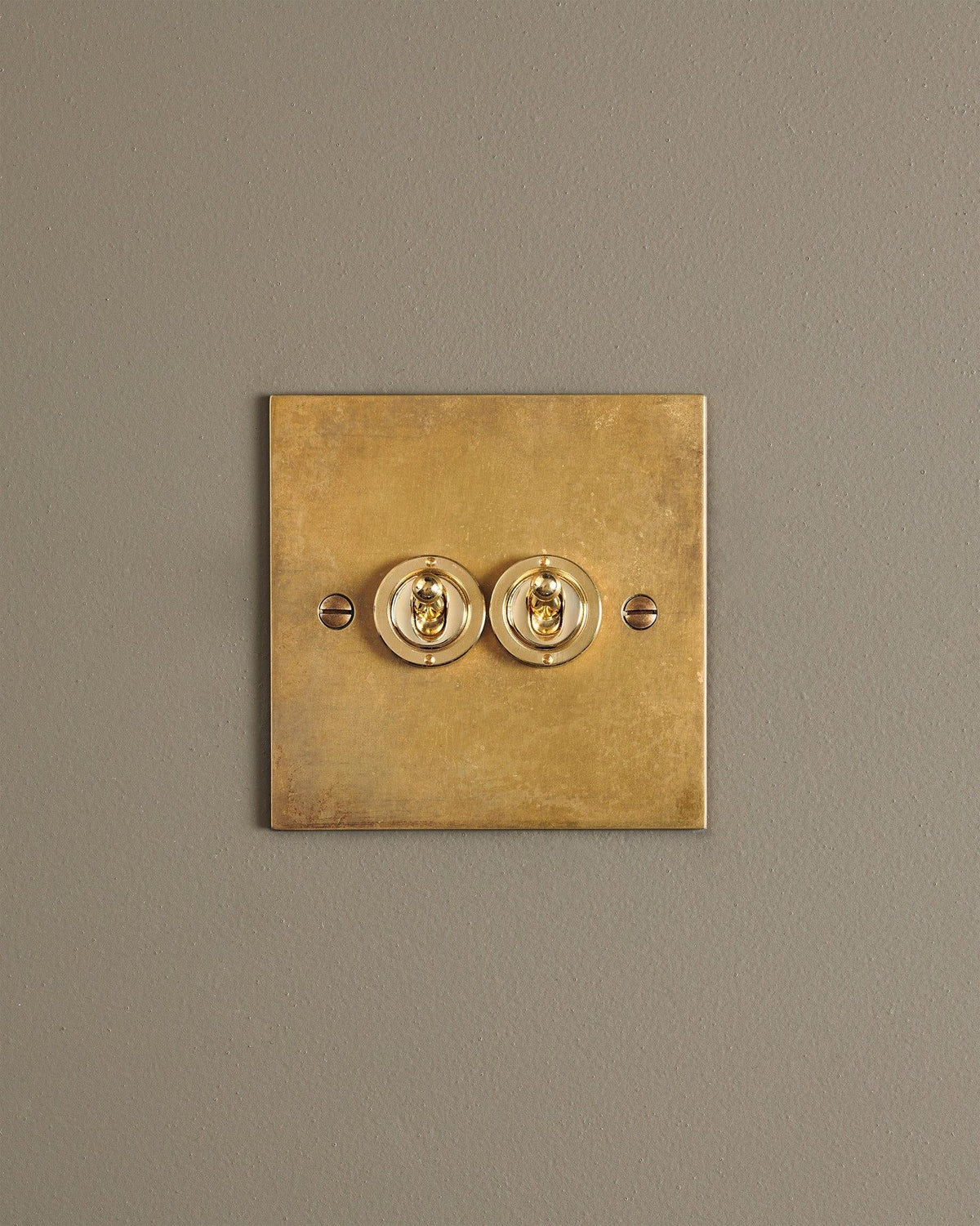 A straight-on view of a 2 gang classic toggle switch in a warm burnished brass finish. TEST