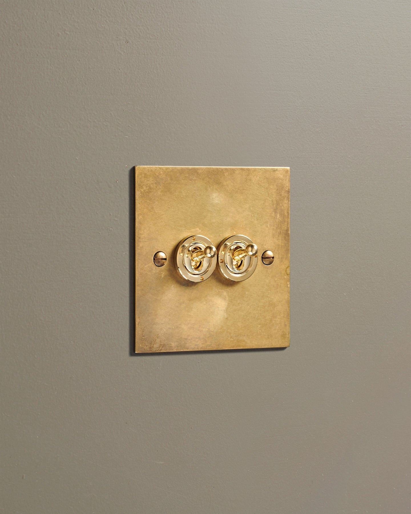 An oblique view of a 2 gang classic toggle switch in a warm burnished brass finish.