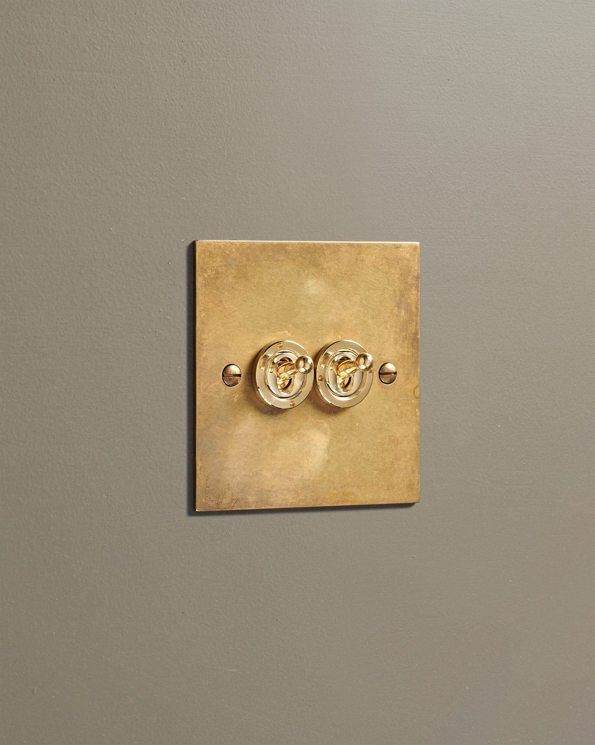 An oblique view of a 2 gang classic toggle switch in a warm burnished brass finish. TEST