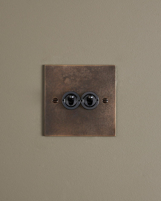 A straight-on view of a 2 gang classic toggle switch in a dark oxidised brass finish.