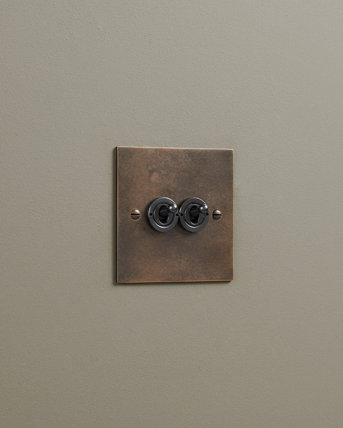 An oblique view of a 2 gang classic toggle switch in a dark oxidised brass finish. TEST