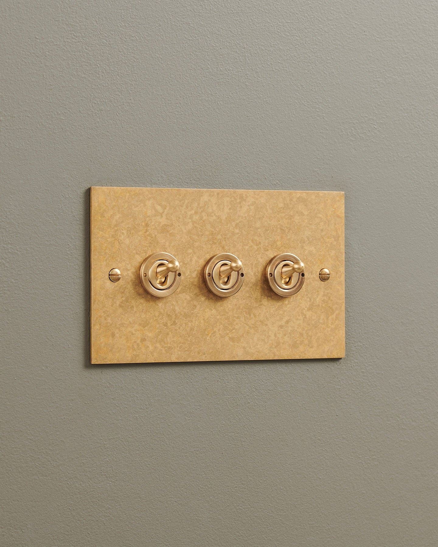 An oblique view of a 3 gang classic toggle switch in a mottled aged brass finish.