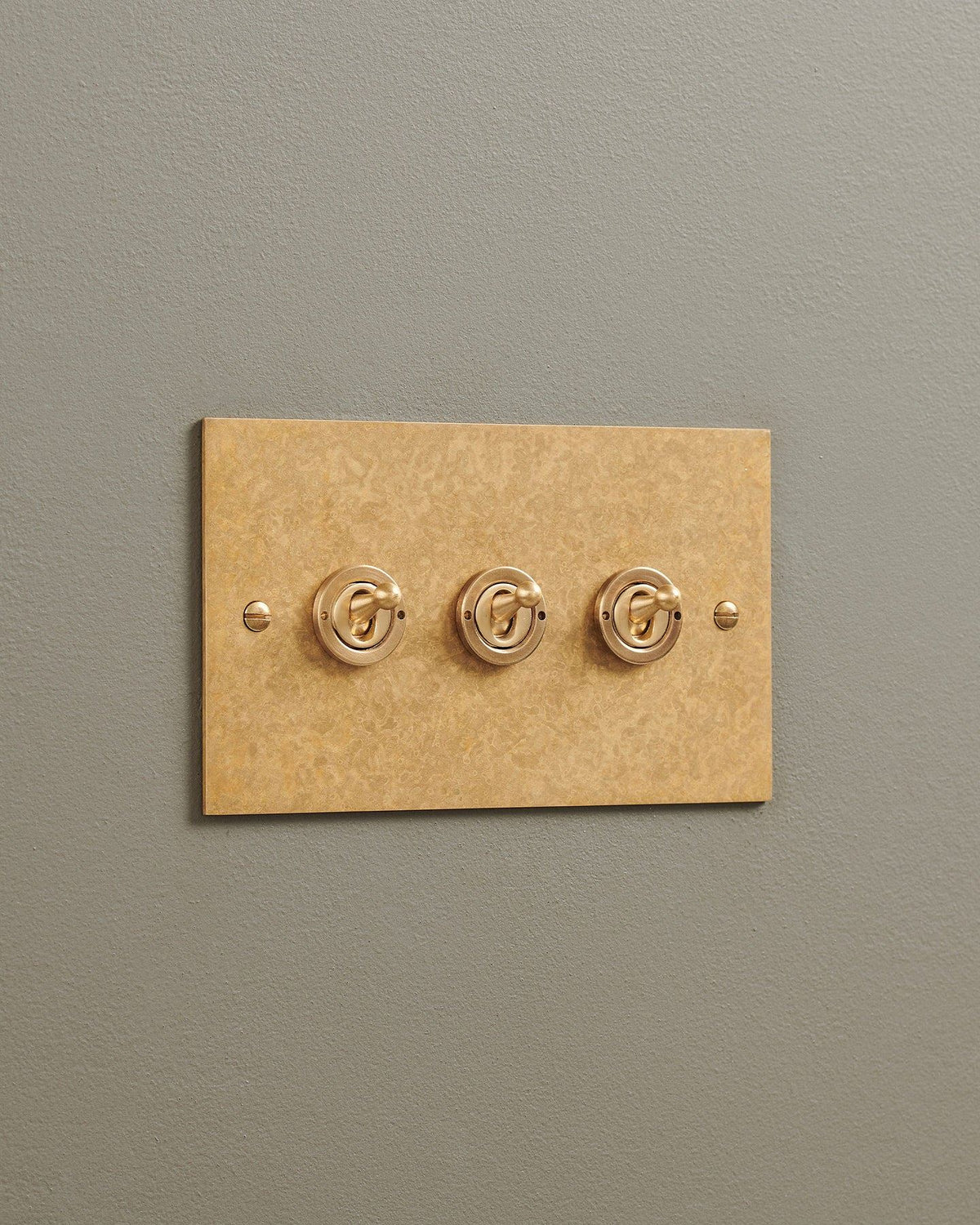 An oblique view of a 3 gang classic toggle switch in a mottled aged brass finish. TEST