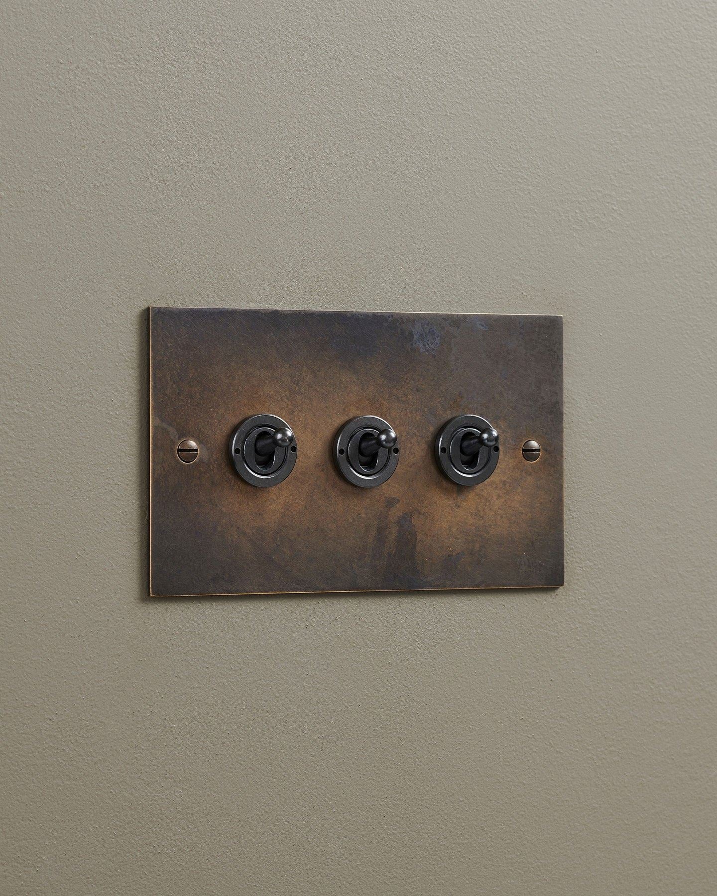 An oblique view of a 3 gang classic toggle switch in a dark oxidised brass finish.