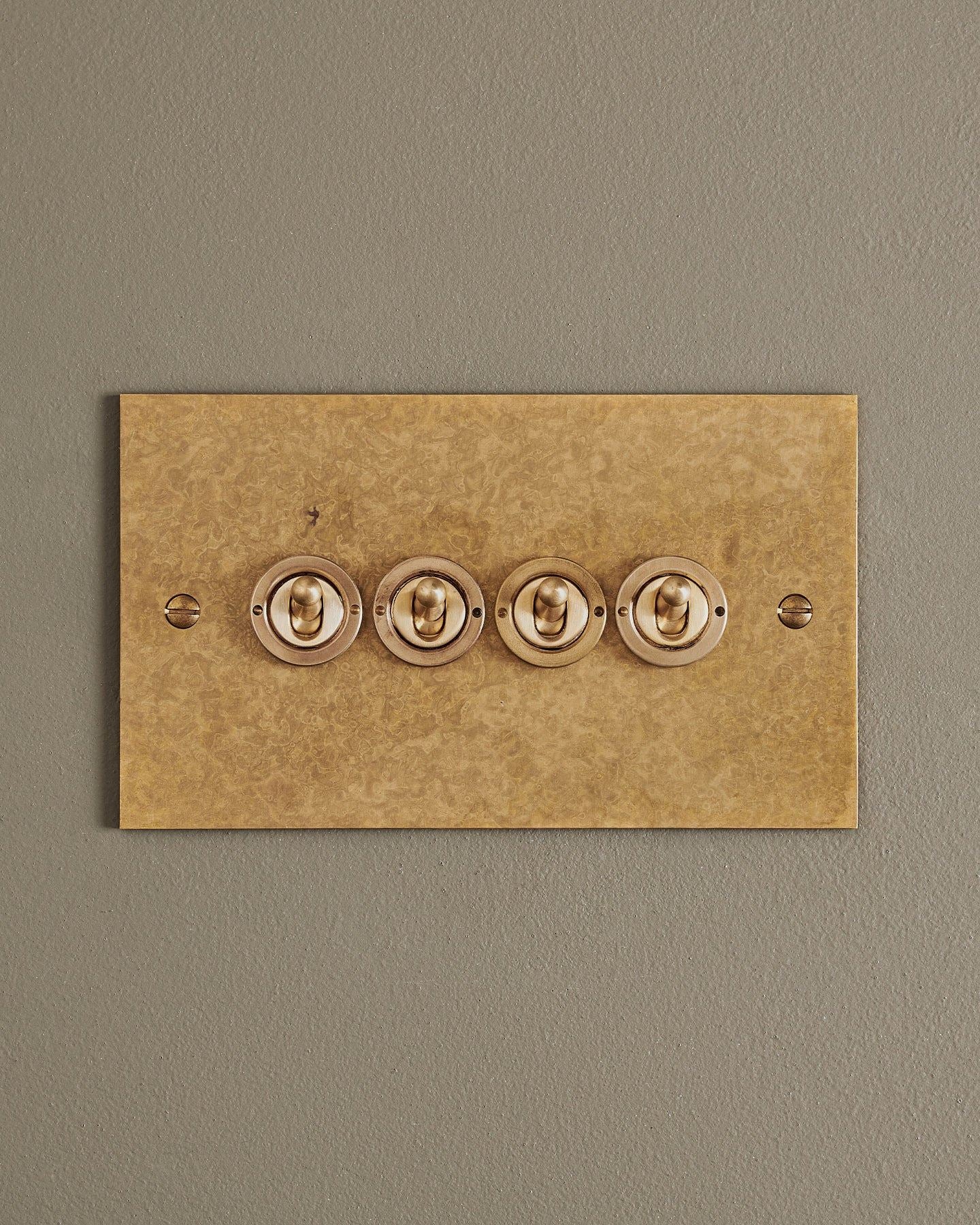 A straight-on view of a 4 gang classic toggle switch in a mottled aged brass finish.