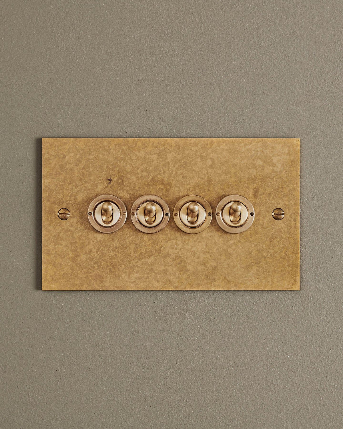 A straight-on view of a 4 gang classic toggle switch in a mottled aged brass finish. TEST