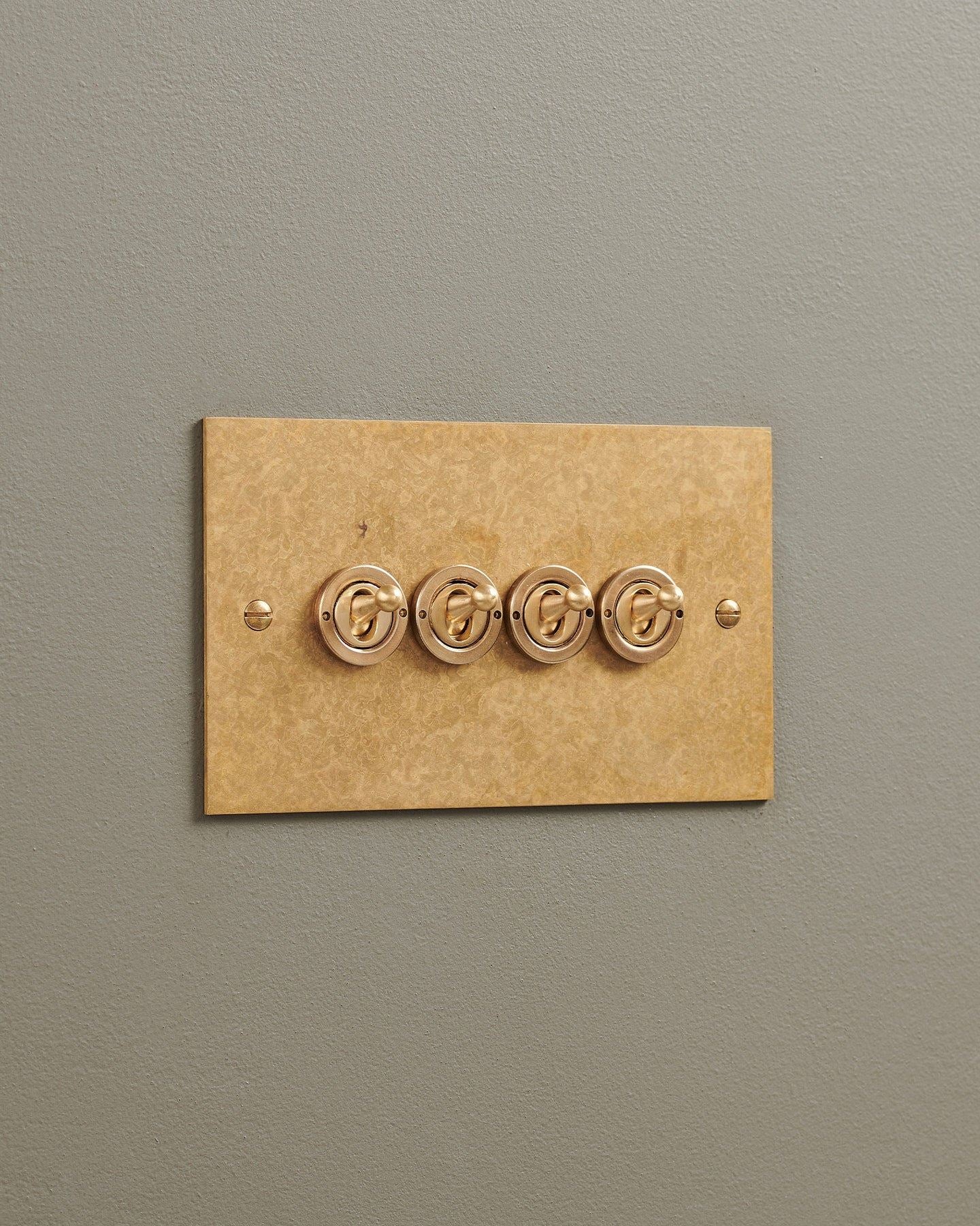 An oblique view of a 4 gang classic toggle switch in a mottled aged brass finish.