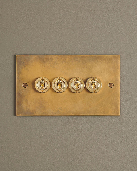 A straight-on view of a 4 gang classic toggle switch in a warm burnished brass finish.