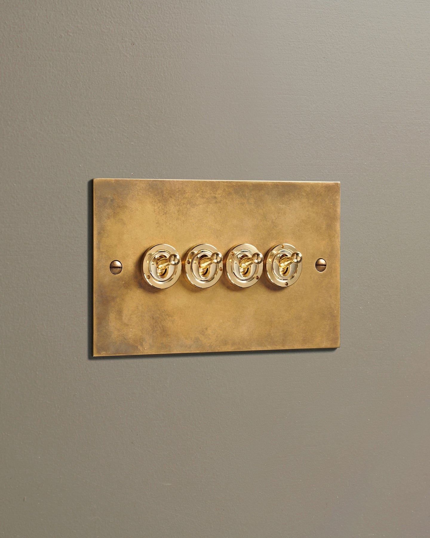 An oblique view of a 4 gang classic toggle switch in a warm burnished brass finish.