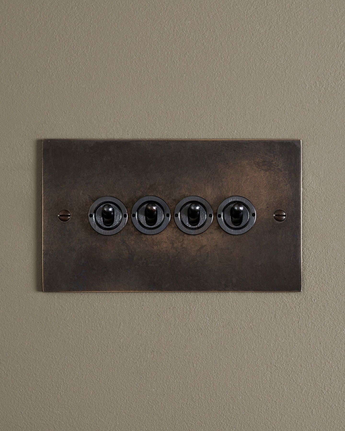 A straight-on view of a 4 gang classic toggle switch in a dark oxidised brass finish.