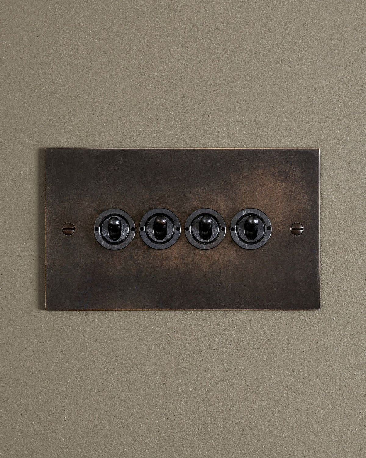 A straight-on view of a 4 gang classic toggle switch in a dark oxidised brass finish. TEST