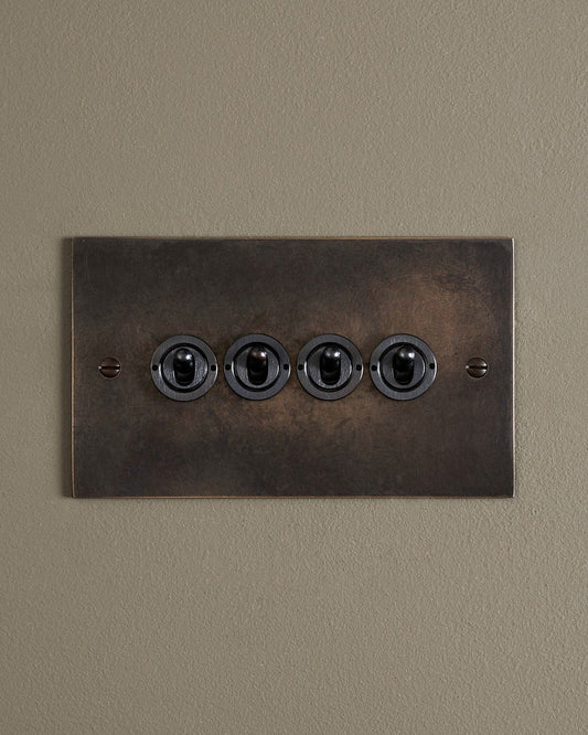 A straight-on view of a 4 gang classic toggle switch in a dark oxidised brass finish.