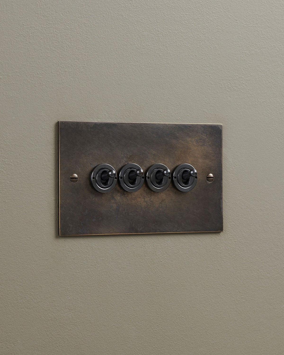 An oblique view of a 4 gang classic toggle switch in a dark oxidised brass finish. TEST
