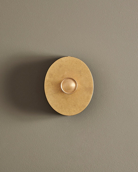 A straight-on view of a small 1 gang oval-shaped dimmer switch in a mottled aged brass finish with a black base.