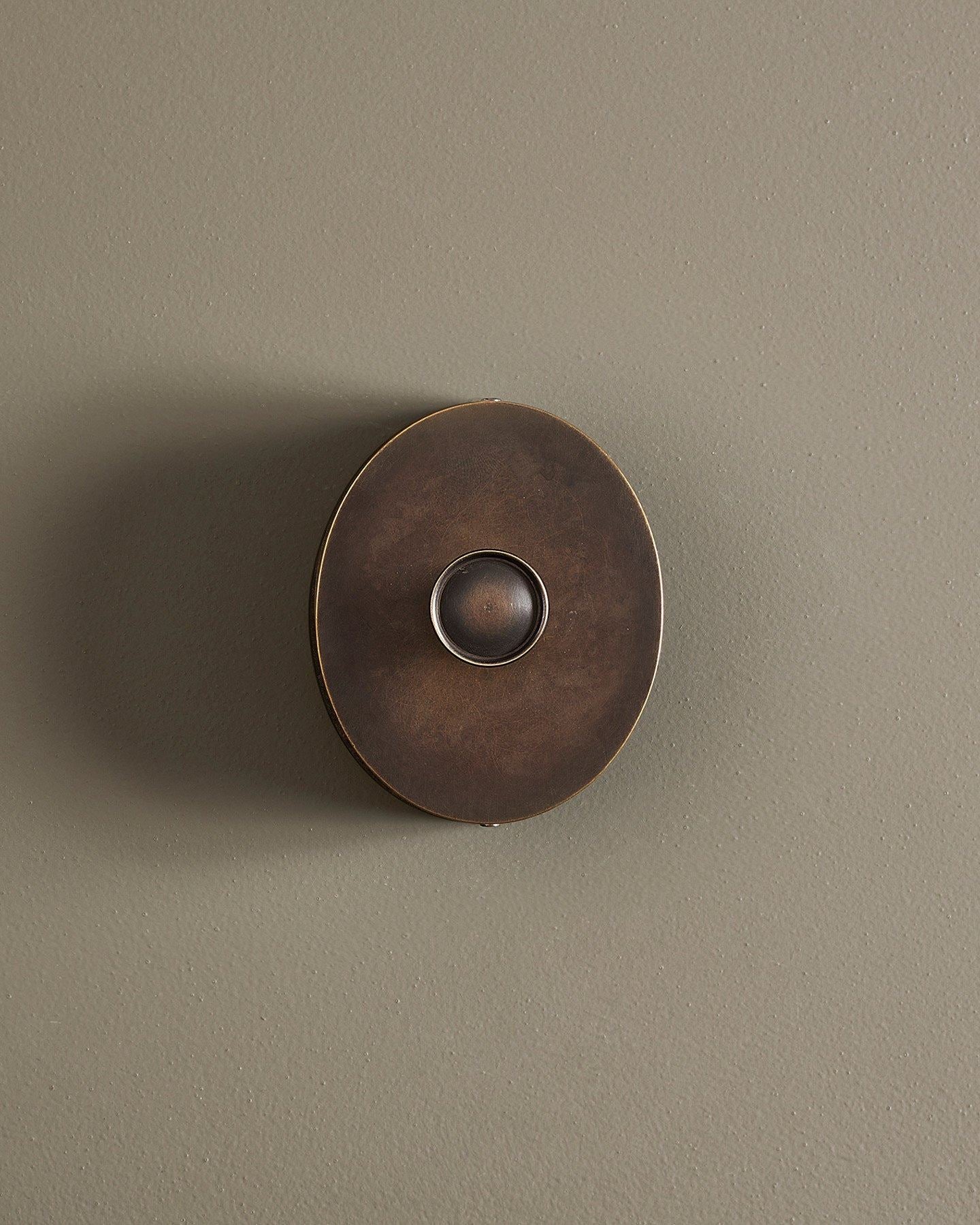 A straight-on view of a small 1 gang oval-shaped dimmer switch in a dark oxidised brass finish with a black base.