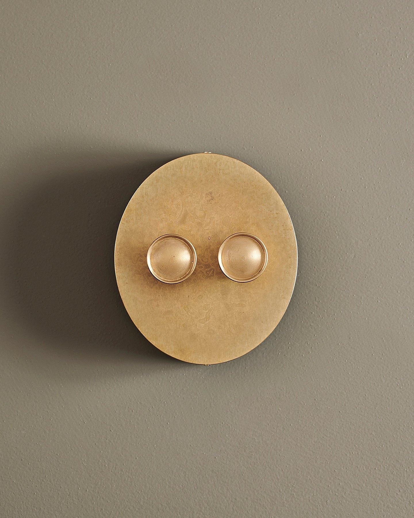 A straight-on view of a 2 gang oval-shaped dimmer switch in a mottled aged brass finish with a black base.