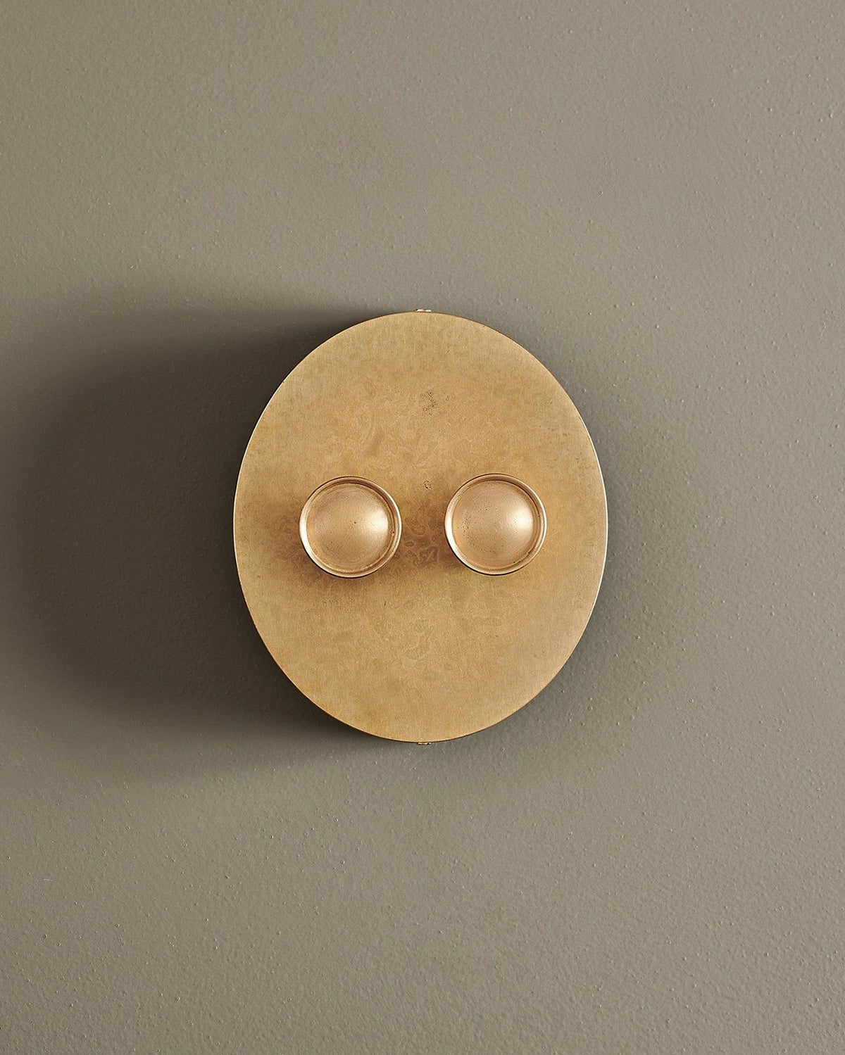 A straight-on view of a 2 gang oval-shaped dimmer switch in a mottled aged brass finish with a black base. TEST