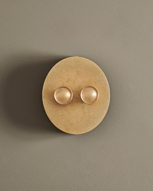 A straight-on view of a 2 gang oval-shaped dimmer switch in a mottled aged brass finish with a black base.