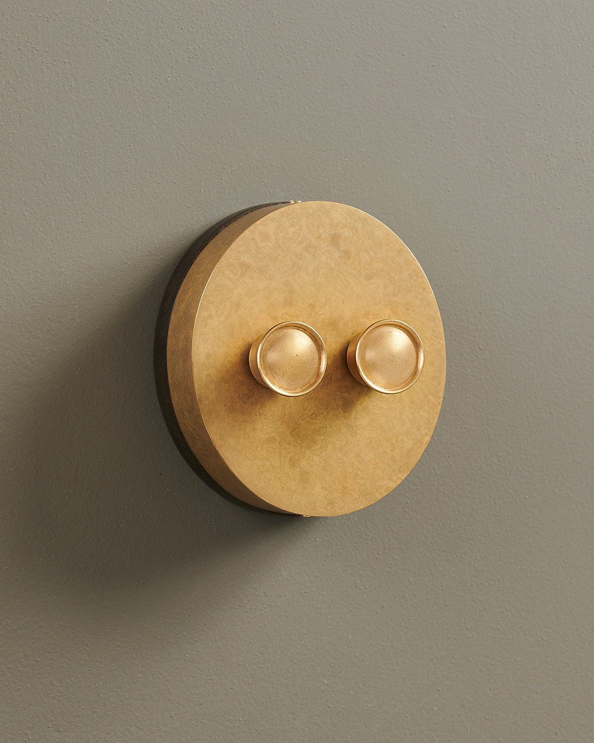 An oblique view of a 2 gang oval-shaped dimmer switch in a mottled aged brass finish with a black base. TEST