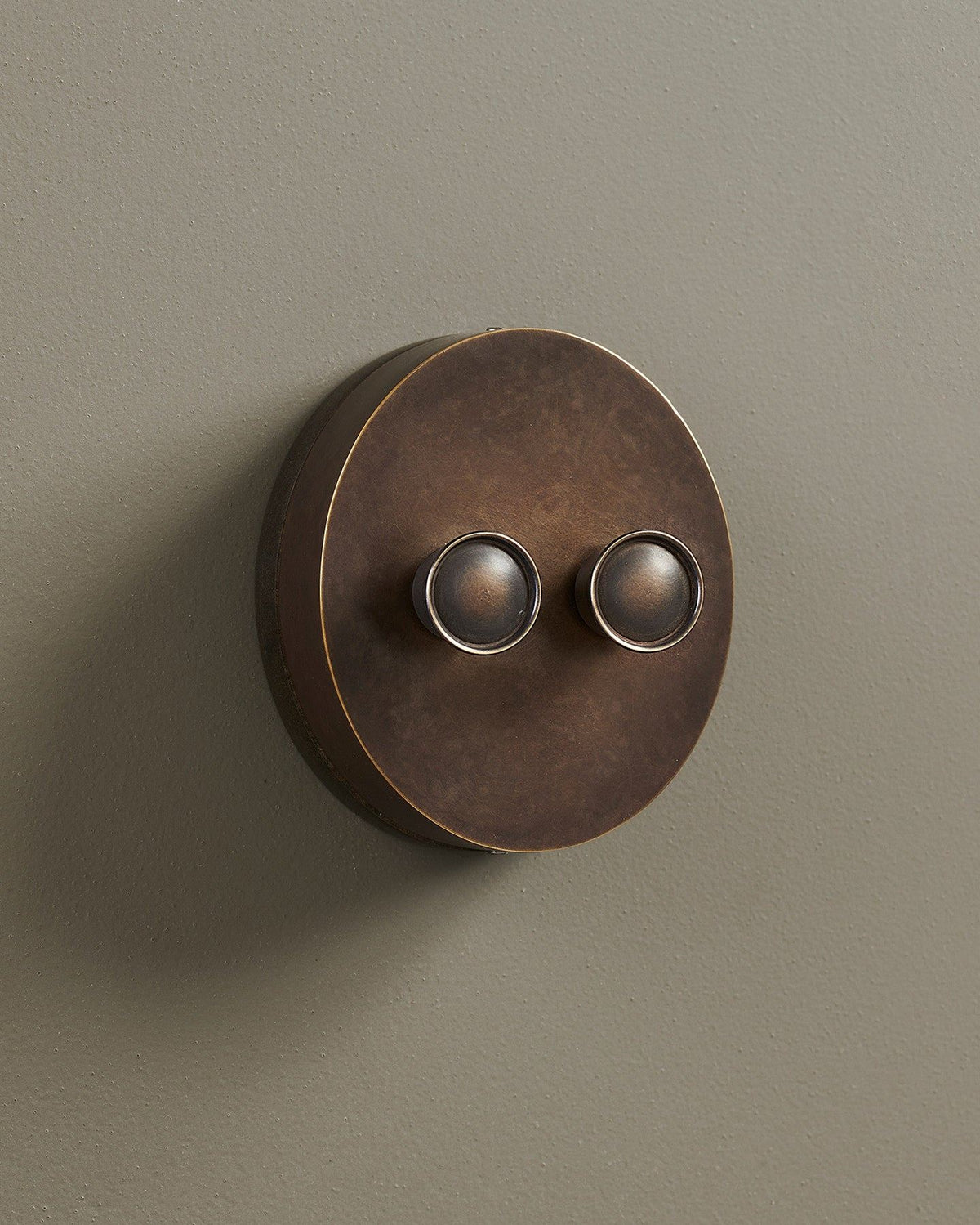 An oblique view of a 2 gang oval-shaped dimmer switch in a dark oxidised brass finish with a black base. TEST