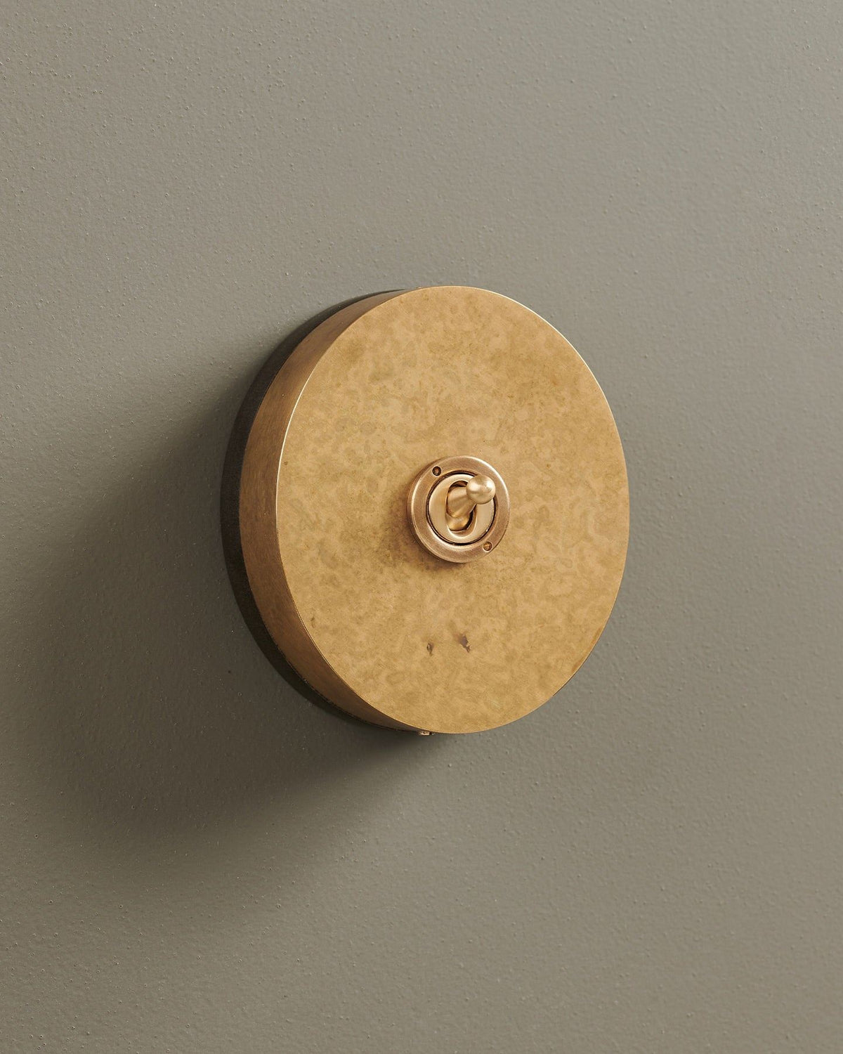 An oblique view of a 1 gang oval-shaped toggle switch in a mottled aged brass finish with a black base. TEST