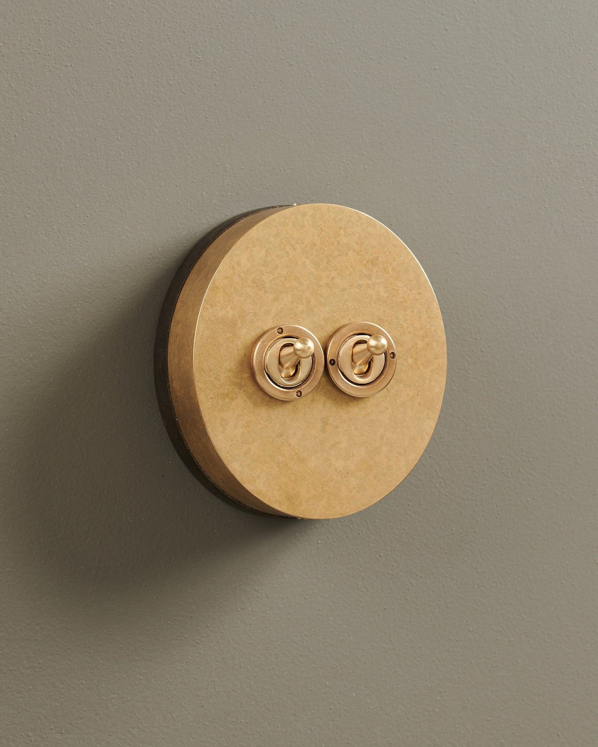 An oblique view of a 2 gang oval-shaped toggle switch in a mottled aged brass finish with a black base. TEST