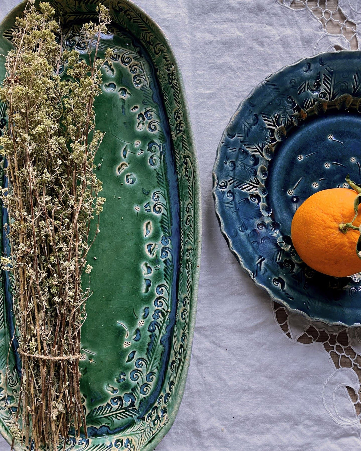 An overhead view of a green oval-shaped ceramic platter and a blue round-shaped ceramic platter with a single orange on top. TEST