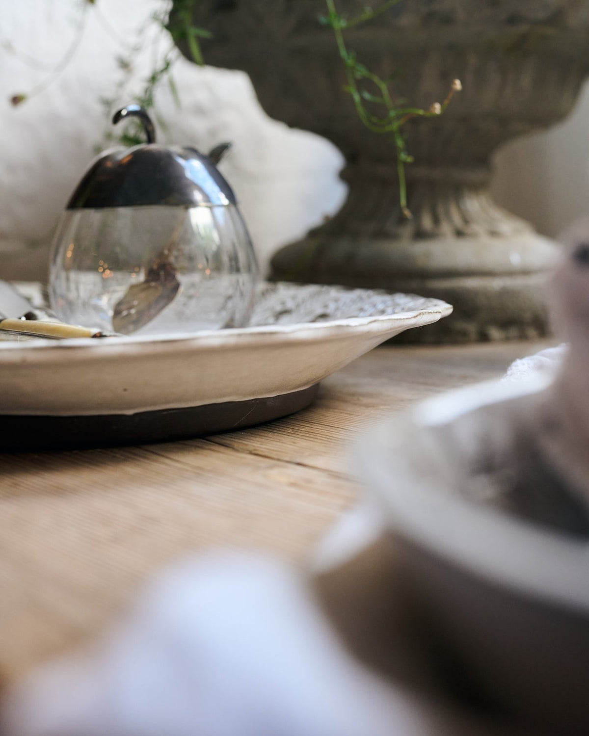 A profile view of a round handmade bohemian-style white ceramic platter on a vintage farmhouse table. TEST