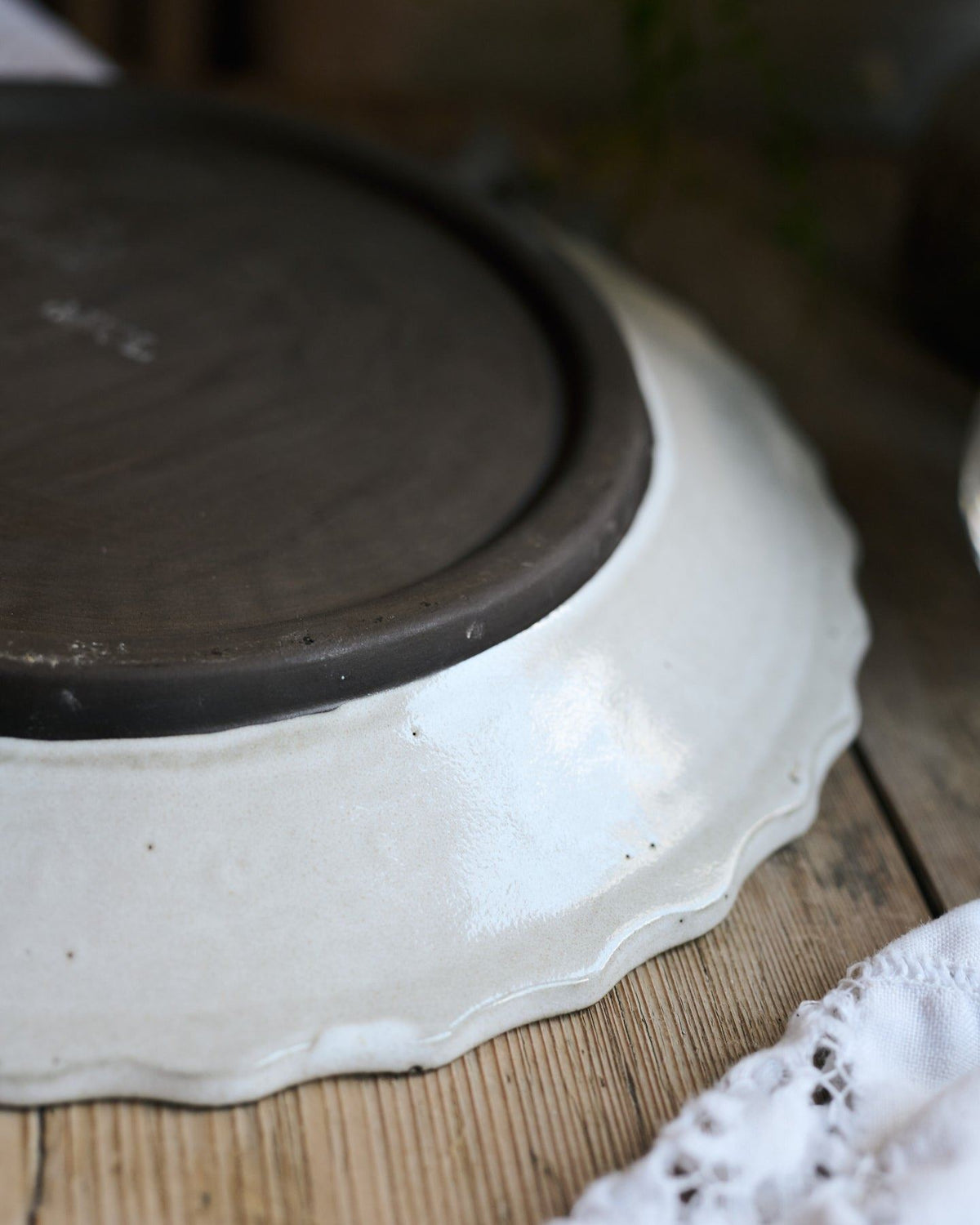 A close-up view of the underside of a white glazed rim and unglazed clay foot of a handmade bohemian-style ceramic platter. TEST