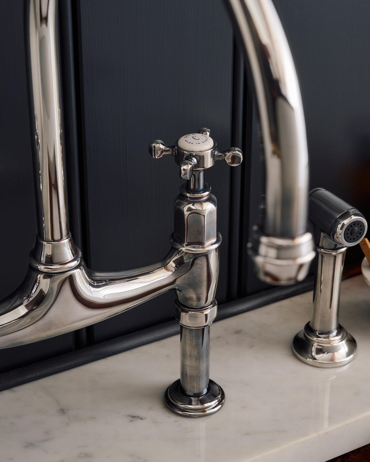 A close-up view of the spout of a traditional-style tarnished silver mixer tap with crosshead handles.