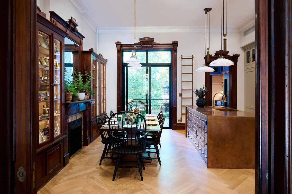 A grand and spacious classic English kitchen features a half vintage and half deVOL kitchen island with a copper sink and worktop. Beautifully decorated with a solid oak dining table set, luscious green house plants, artisan ceramics, a bespoke ladder, and milk glass pendant lights, it creates a social space with a touch of luxury.