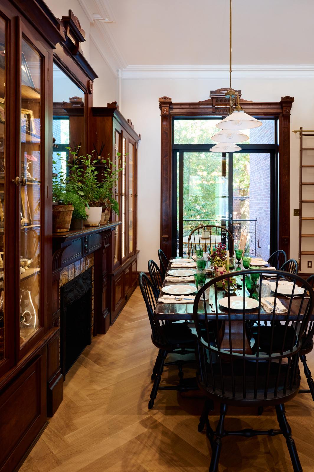 This grand and spacious classic English kitchen is beautifully decorated with a solid oak dining table set, lush green house plants, artisan ceramics, a bespoke ladder, and milk glass pendant lights. Together, these elements create a social space that exudes a touch of luxury.
