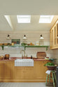 The quaint and glamorous cottage kitchen, in shades of green and scullery yellow, includes a small sink run with an oak countertop, an aged brass Ionian tap, and glazed wall cabinets. Lovingly decorated with vintage furniture, ceramics, luscious vegetables, and three deVOL mini creamware wall lights, the space exudes personality and charm while respecting the cottage's original textures.