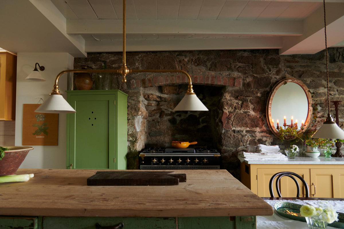 The quaint and glamorous cottage kitchen, in shades of green and scullery yellow, includes a freestanding cupboard and a marble-topped base cabinet. Lovingly decorated with vintage furniture, ceramics, and deVOL Heirloom gaselier lights, the space exudes personality and charm while respecting the cottage's original textures.