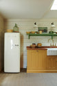 A quiet corner of a quaint and glamorous cottage kitchen, in shades of green and scullery yellow, includes a small sink run with an oak countertop, an aged brass Ionian tap, and a Smeg fridge. Lovingly decorated with vintage furniture, ceramics, luscious vegetables, and three deVOL mini creamware wall lights, the space exudes personality and charm while respecting the cottage's original textures.