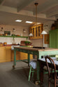 The quaint and glamorous cottage kitchen, in shades of green and scullery yellow, includes a small sink run with an oak countertop, an aged brass Ionian tap, glazed wall cabinets, freestanding cupboards, and a marble-topped base cabinet. Lovingly decorated with vintage furniture, ceramics, and deVOL Heirloom gaselier lights, the space exudes personality and charm while respecting the cottage's original textures.