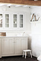 A beautiful white linen kitchen features a cooker run with a Carrara marble worktop, glazed wall cupboards, and a collection of vintage furniture and items reflecting on the well-reserved historical space with its original plastered walls, wooden beams and oak floors.