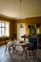 A closer look at a lovely modern kitchen that retains the charm of its original structure and flooring, using the three primary colours in a muted, mature palette. The spacious kitchen features an emerald green gas stove sits within the chimney breast, accompanied by a deVOL cream pendant light above a vintage round wooden table, with matching chairs and a prep table.