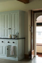 This simple and spacious classic English kitchen features a free-standing closed larder pantry cupboard. Adorned with simple ceramics, tea towels, and basic cooking utensils, it creates a humble and functional family kitchen.