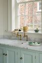 A closer look at a humble and calming turquoise, classic English kitchen’s single sink with an aged brass Mayan taps, Carrara marble worktop. Adorned with fresh eggs on an emerald oval plate, artisan ceramics, and wooden cleaning equipments, it creates a warm and simple home kitchen.
