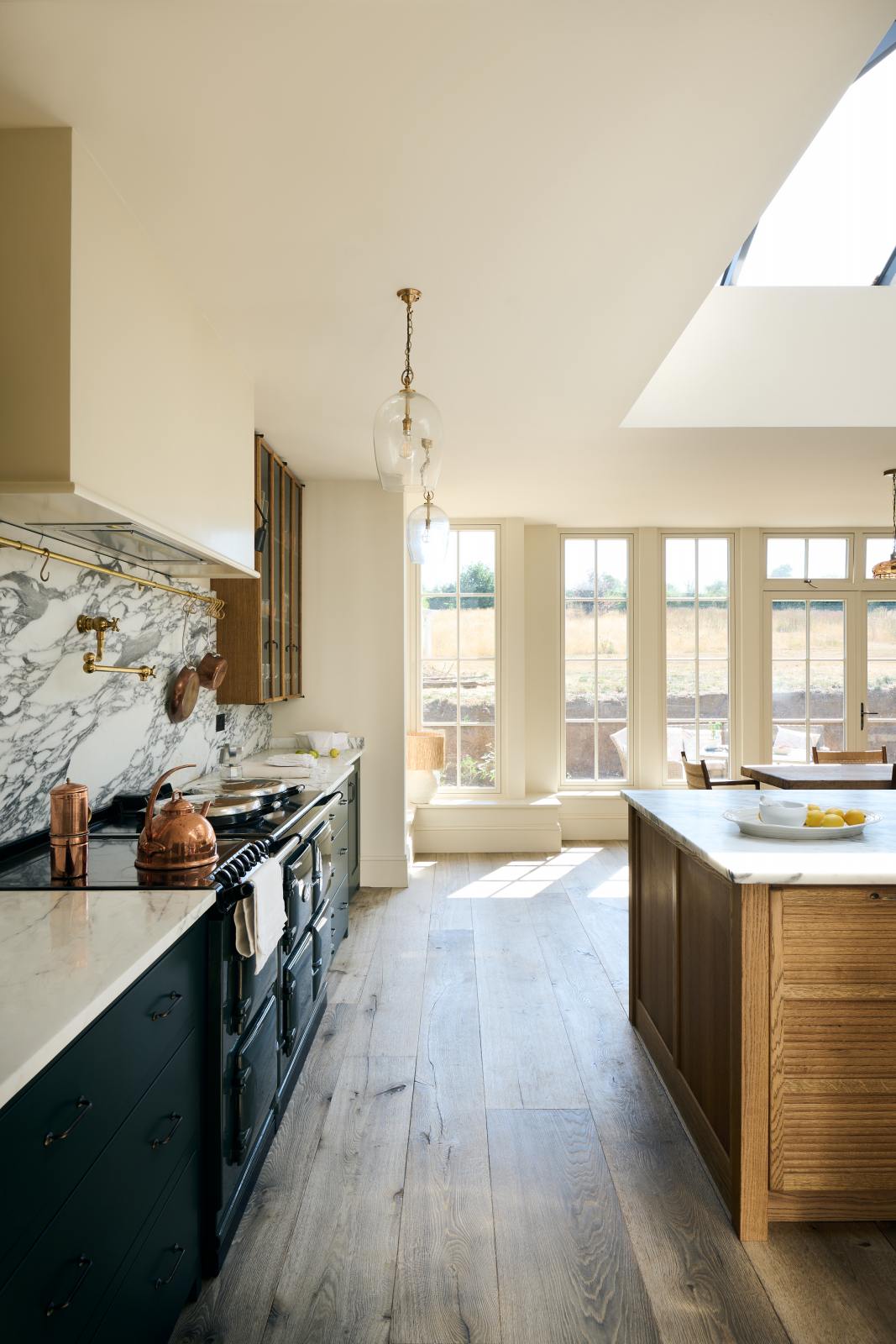 Nestled between the elegant and spacious Haberdasher’s kitchen, which features a large cooker run and a kitchen island with an Arabescato marble worktop, splashback, and glazed cupboards, is a long window wall that lets in bright white light. Adorned with vintage furniture, artisan ceramics, glass flower pendant lights, and a sunflower arrangement, this kitchen creates a classic social space with functional storage.